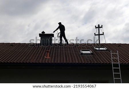 A chimney sweep cleans the chimney on a house roof Royalty-Free Stock Photo #2193554067