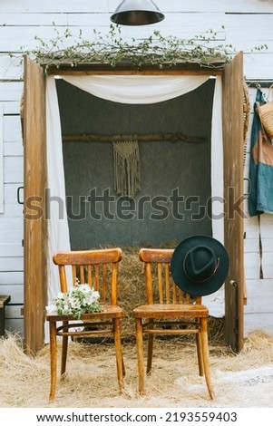 empty chairs with hat and bouquet of bride near barn of country house at boho style wedding celebration, boho decorations with macrame and hay, mock up