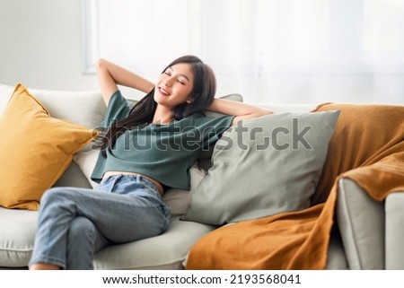 Relaxed young asian woman enjoying rest on comfortable sofa at home, calm attractive girl relaxing and breathing fresh air in home, copy space. Royalty-Free Stock Photo #2193568041