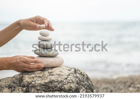 Tanned woman hands stacked pebble stones tower on sea beach relaxing harmony summer travel vacation. Female arms pillar formation peaceful balance pyramid spa spiritual gravel cobblestone at seaside Royalty-Free Stock Photo #2193579937