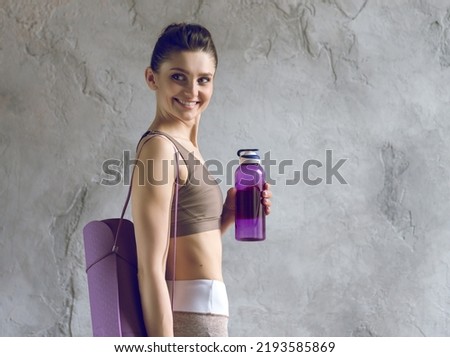 Sporty Young Woman Holding a Bottle of Water and Carpet for Yoga Training.