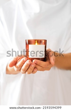 Woman in white clothing holding burning candle close-up. Mock up for candle shop. Space for text or logo branding. Stories format advertising aromatherapy or candle handmade masterclass. Church poster