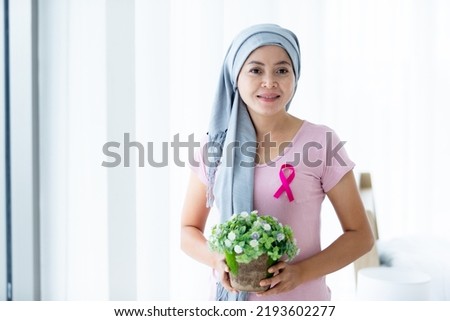 Portrait of a asian women disease mammary cancer patient Holding flower pots with pink ribbon wearing headscarf After treatment to chemotherapy at the window In the bedroom at the house