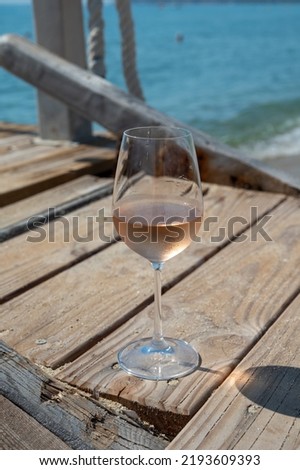 Glasses of cold rose wine from Provence served outdoor on wooden yacht pier with view on blue water and white sandy beach Plage de Pampelonne near Saint-Tropez, summer vacation in France