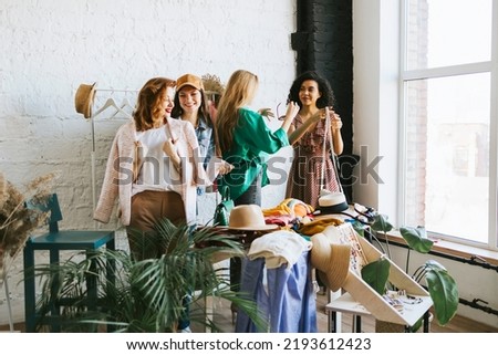 four young woman female caucasian and african students at swap party try on clothes, bags, shoes and accessories, change clothes with each other, second hand for things, zero waste life, eco-friendly Royalty-Free Stock Photo #2193612423