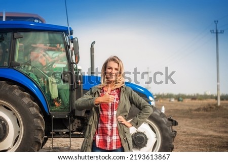Pretty smiling woman with positive emotions on the background of a tractor in a field.