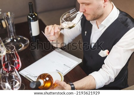 Wine waiter smells white drink in wineglass in winehouse. Royalty-Free Stock Photo #2193621929