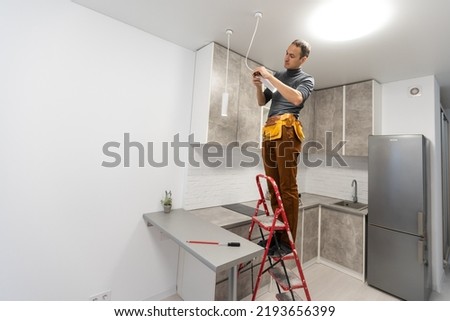 electrician, a male electrician is standing on the stairs holding wiring in his hands and stripping, repairing light at home, repair work, call master, electrician man repairing light Royalty-Free Stock Photo #2193656399