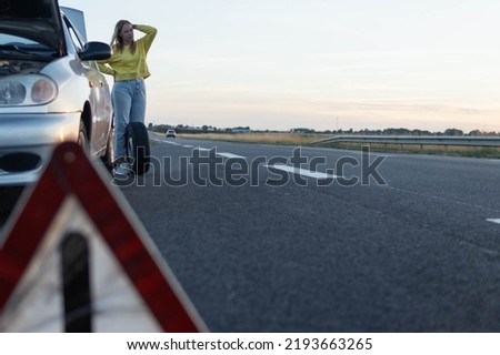 girl in stands near the rear wheel of the car and rolls a spare wheel to change it.A car breakdown, the wheel in front is a temporary stop sign blurred on the right there is a place for an Royalty-Free Stock Photo #2193663265