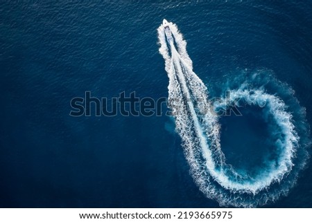 Aerial top view of a motor powerboat forming a circle of waves and bubbles with its engines over the blue sea Royalty-Free Stock Photo #2193665975