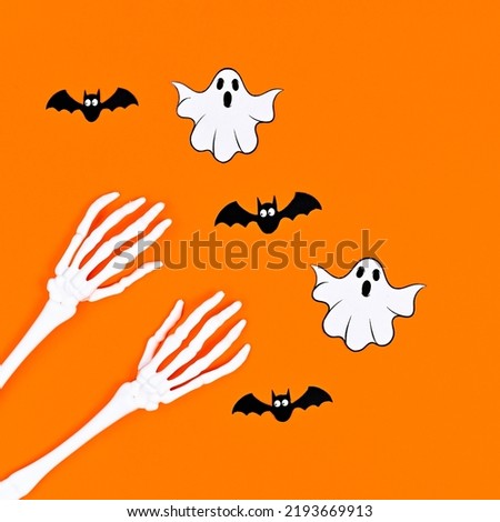 Skeleton hands with bats and ghosts on orange background. Flat lay