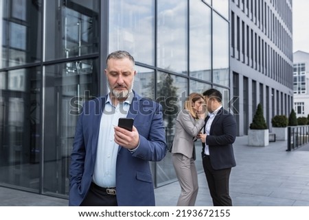 Two colleagues are gossiping at background behind the boss. workmate about bullying problem at work place in office in the break outside Male Coworkers employees man and woman Whispering Behind Back Royalty-Free Stock Photo #2193672155