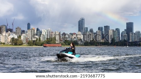 Adventurous Caucasian Woman on Water Scooter riding in the Ocean. Modern City in background. Downtown Vancouver, British Columbia, Canada.