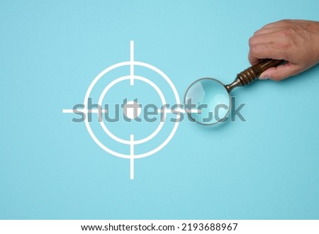 Female hand holding wooden magnifier and target icon on blue background