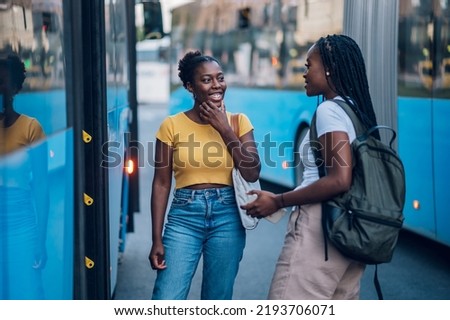 African american female friends waiting for a bus while at a bus stop. Riding, sightseeing, traveling to work, city tour, togetherness. Two black woman entering the public transport.