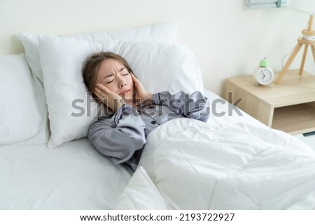 Caucasian beautiful frustrated girl in pajamas sleep on bed in morning. Attractive young woman lying down with upset and angry feeling due to noise and put cozy blanket on her ears in bedroom in house Royalty-Free Stock Photo #2193722927