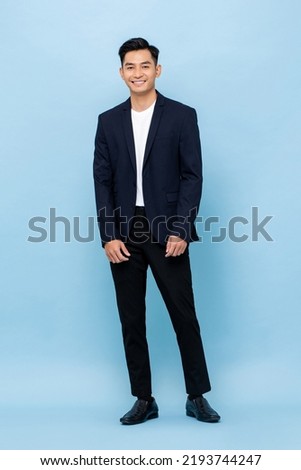 Young handsome southeast Asian man wearing semi-formal suit smiling and looking at camera in blue color studio isolated background