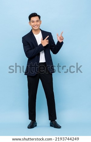 Young handsome smiling Asian man wearing semi-formal suit looking at camera and pointing hands up in blue color studio isolated background Royalty-Free Stock Photo #2193744249