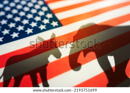 Democrats vs republicans are in a ideological duel on the american flag. In American politics US parties are represented by either the democrat donkey or republican elephant. animal shadows on flag