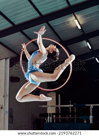 Sports woman, performance and ring in the air for gymnastics show. Fitness girl doing artistic pose and stretch for acrobat stunt. Young and beautiful athlete in gym with hula hoop and flexible body