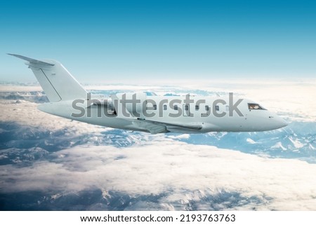 White modern executive jetliner flies over snow-covered mountains