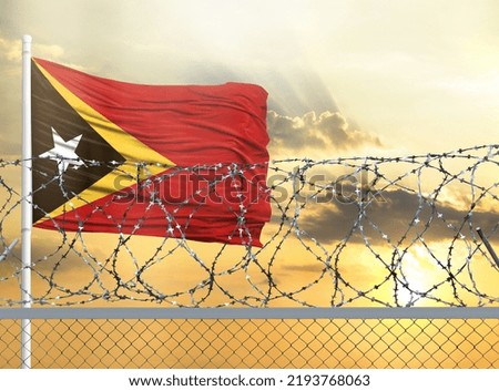 Flagpole with the flag of East Timor against the sky and behind a fence with barbed wire. The concept of protecting the borders of territories.