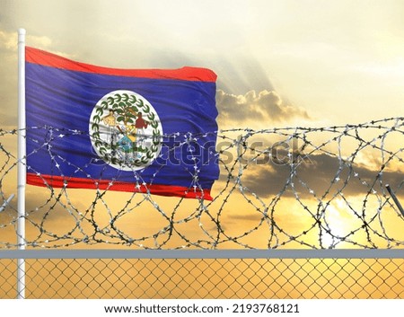 Flagpole with the flag of Belize against the sky and behind a fence with barbed wire. The concept of protecting the borders of territories.