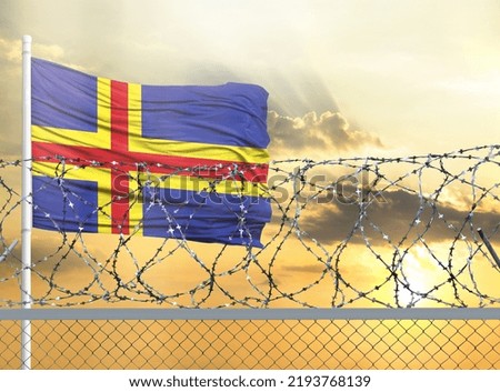 Flagpole with the flag of Aland against the sky and behind a fence with barbed wire. The concept of protecting the borders of territories.