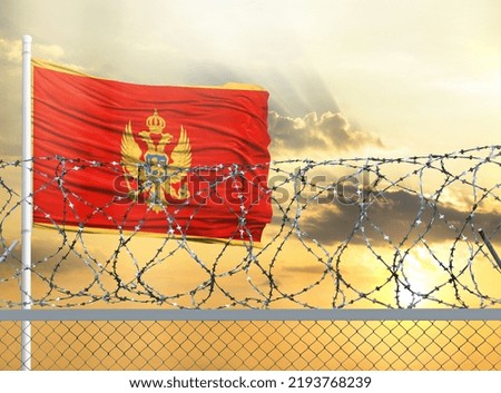 Flagpole with the flag of Montenegro against the sky and behind a fence with barbed wire. The concept of protecting the borders of territories.