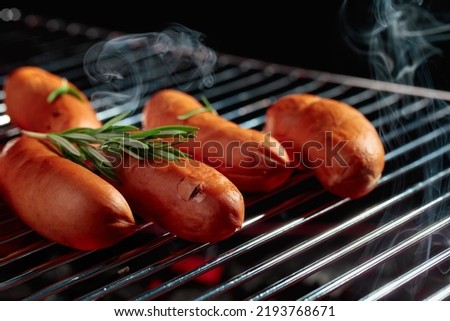 Grilled sausages on a grill with smoke on dark background.