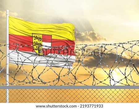 Flagpole with the flag of Carinthia against the sky and behind a fence with barbed wire. The concept of protecting the borders of territories.