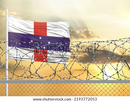 Flagpole with the flag of Netherlands Antilles against the sky and behind a fence with barbed wire. The concept of protecting the borders of territories.