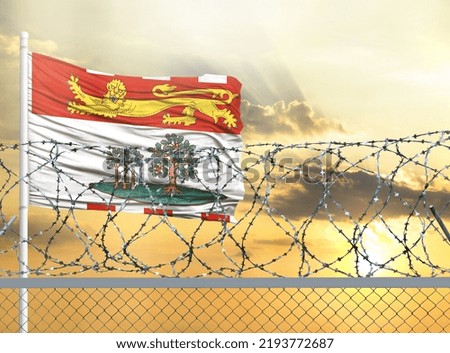 Flagpole with the flag of Prince Edward Island against the sky and behind a fence with barbed wire. The concept of protecting the borders of territories.