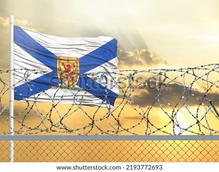 Flagpole with the flag of Nova Scotia against the sky and behind a fence with barbed wire. The concept of protecting the borders of territories.