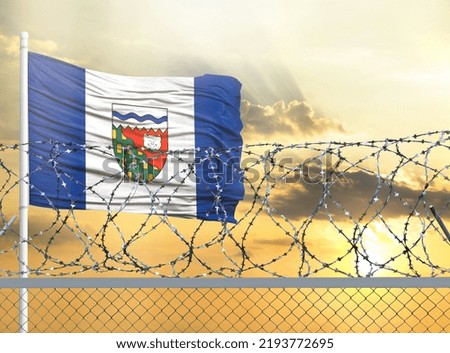 Flagpole with the flag of Northwest Territories against the sky and behind a fence with barbed wire. The concept of protecting the borders of territories.