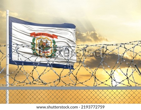 Flagpole with the flag of State of West Virginia against the sky and behind a fence with barbed wire. The concept of protecting the borders of territories.