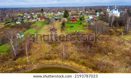 Aerial view of the village on a high hill above the river at sunrise in autumn. Aerial view. Residential buildings and a church, river bends, meadows, orange grass, trees at dawn. 