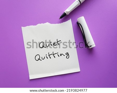 On purple background, pen writing on paper note QUIET QUITTING, when employees not engaged or taking job seriously, do minimum required but focus on job outside office Royalty-Free Stock Photo #2193824977
