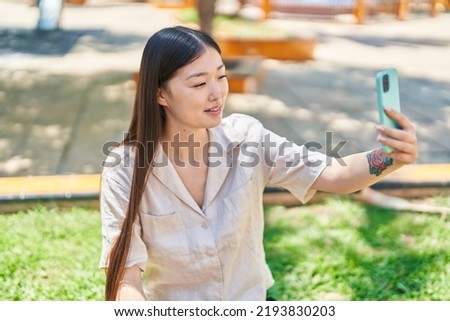 Chinese woman making selfie by the smartphone sitting on grass at park