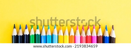 Row of colored pencils on a bright yellow background. Wooden pencils, lined with a color spectrum. Materials for drawing and creativity. Top view, space for text.