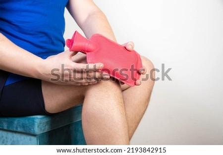 A man attaches a medical heating pad with hot water to his knee. Treatment of knee sprains, pain and inflammation. Thermotherapy Royalty-Free Stock Photo #2193842915