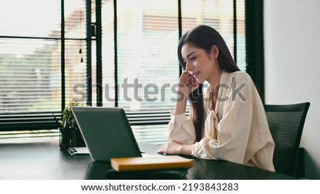 Gorgeous woman entrepreneur sitting in her contemporary office and checking information on laptop