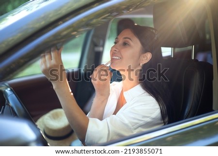 A young beautiful female driver does makeup sits behind the wheel of her car. A modern lady. A trip, a journey. Lifestyle High quality photo