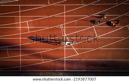 Athlete is on the starting line to start sprinting. parallel lines are around him and it is sunset. his training equipment is behind him