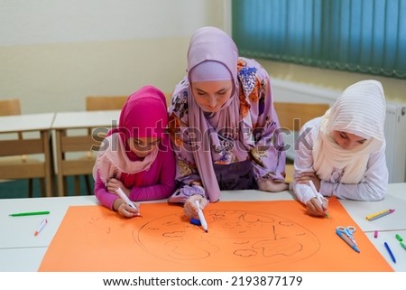 Group of happy Muslim school children with their teacher working on project together at classroom.	
