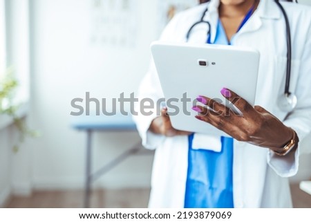 Close up of woman doctor hands using digital tablet at clinic. Closeup of female doctor in labcoat and stethoscope holding digital tablet, reading patient report. Hands holding medical report