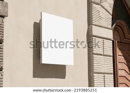 Empty white signage with dark shadow hanging on concrete wall of urban building. Logotype and branding commercial concept.