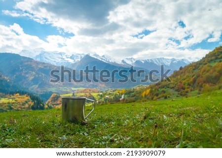 Close-up of a metal mug of hot coffee against the background of beautiful autumn mountains on a sunny day, copy the space. Concept of active tourism, travel