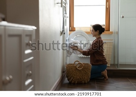 Laundry day. Happy millennial Indian woman renter tenant using modern domestic washing machine for easy laundering of dirty clothes. Satisfied young Hindu lady customer take clean cloth out of dryer Royalty-Free Stock Photo #2193917701