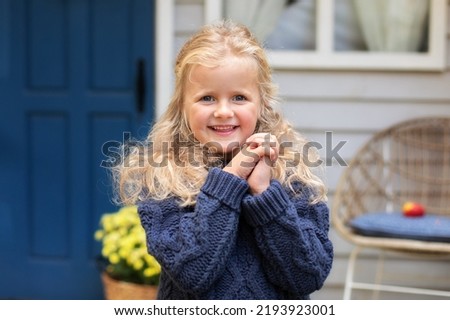 Happy smiling fun little blond hair girl in blue pullover in fall garden. Portrait child praying. Little girl hand praying, hands folded in prayer concept for faith, spirituality and religion.